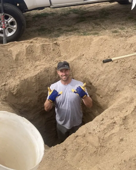 Travis Tompkins grinning with two thumbs up from a trench he dug for an underground electrical run